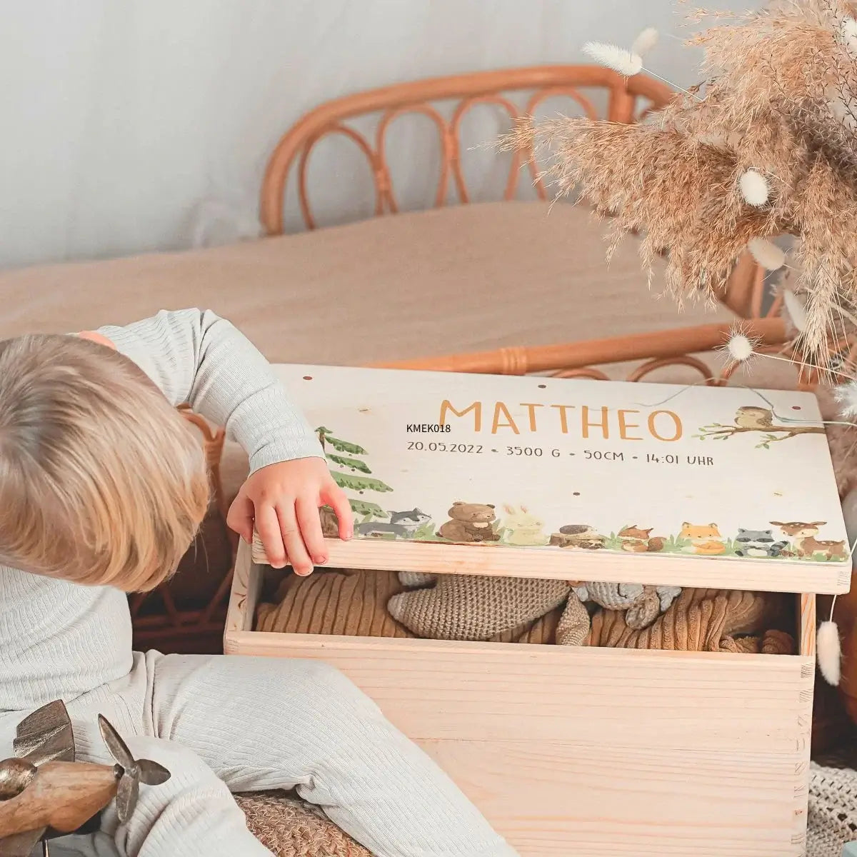 Glückliches Kleinkind präsentiert seine personalisierte Erinnerungsbox aus Holz mit Namen und süßen Waldtier-Motiven als Geburtsgeschenk