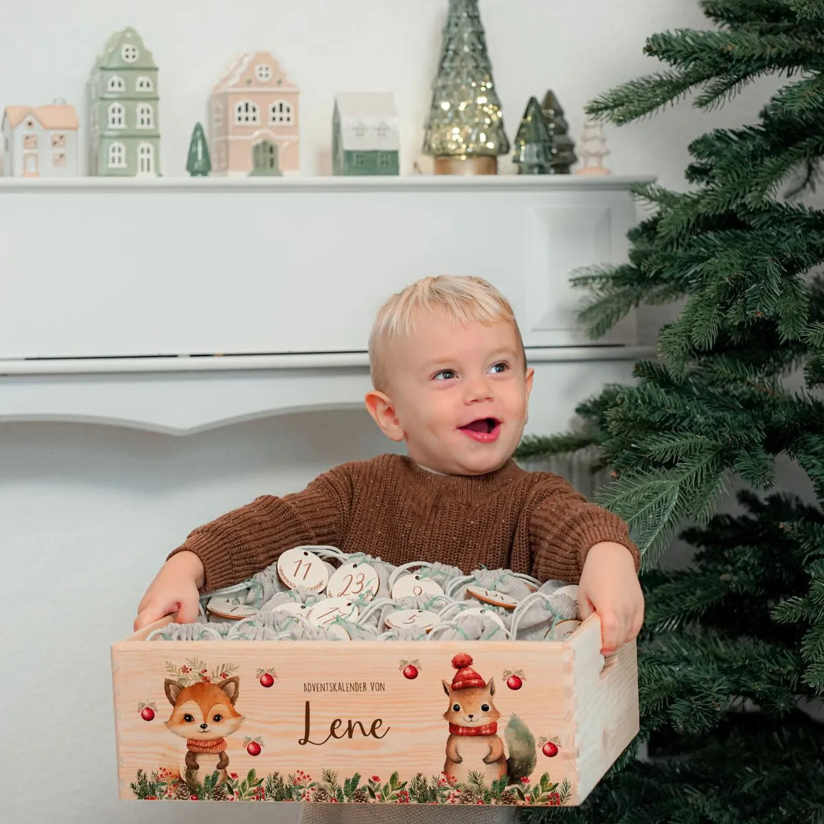Kleiner Junge mit strahlendem Lächeln hält seine Überraschung aus dem personalisierten Adventskalender - festliche Szene mit weihnachtlich dekoriertem Holzkalender zum Selbstbefüllen