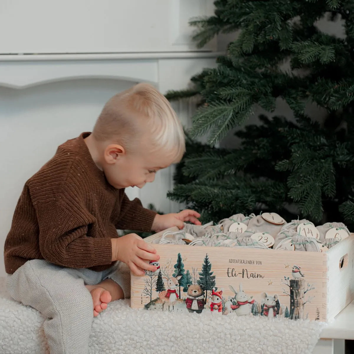 Aufgeregter Junge öffnet Türchen an seinem personalisierten Adventskalender - Kind entdeckt freudig die tägliche Überraschung in seinem Weihnachtskalender mit Namensschild