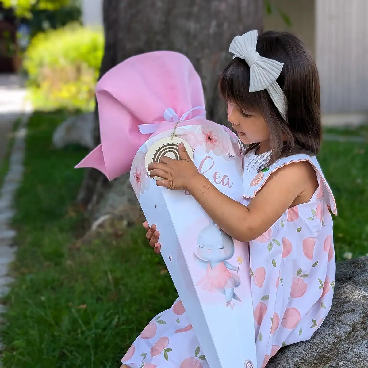 Lächelndes Mädchen mit Einhorn-Schultüte zur Einschulung - fröhliche Erstklässlerin hält ihre personalisierte Schultüte mit Glitzerverzierung und Schleife