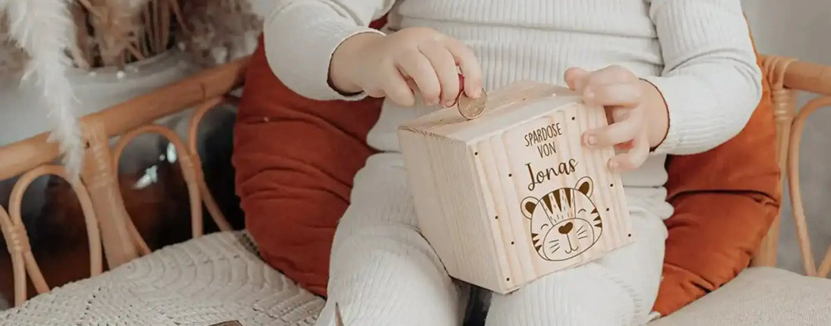 Kind sitzt im Kinderzimmer und wirft Münze in personalisierte Holz-Spardose mit Tiger-Motiv und eigenem Namen